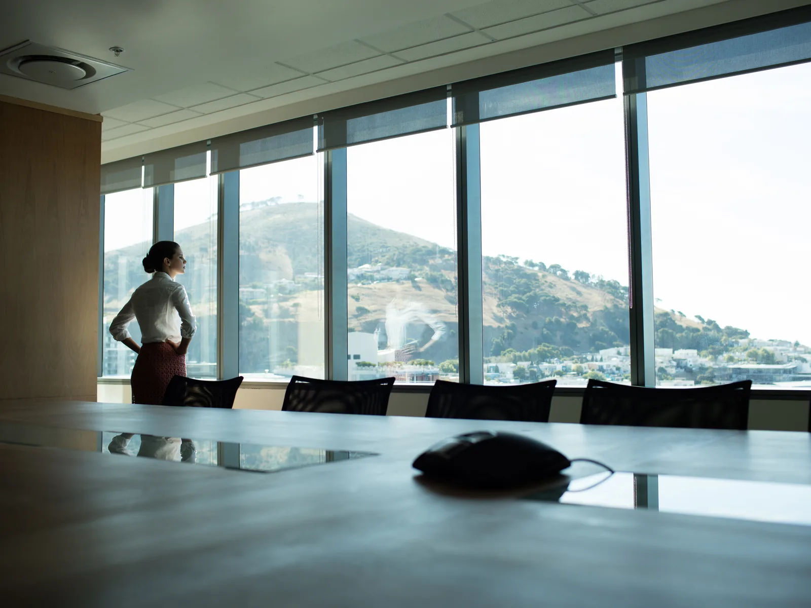 A leader standing at a boardroom window, looking out over the city and the hills beyond